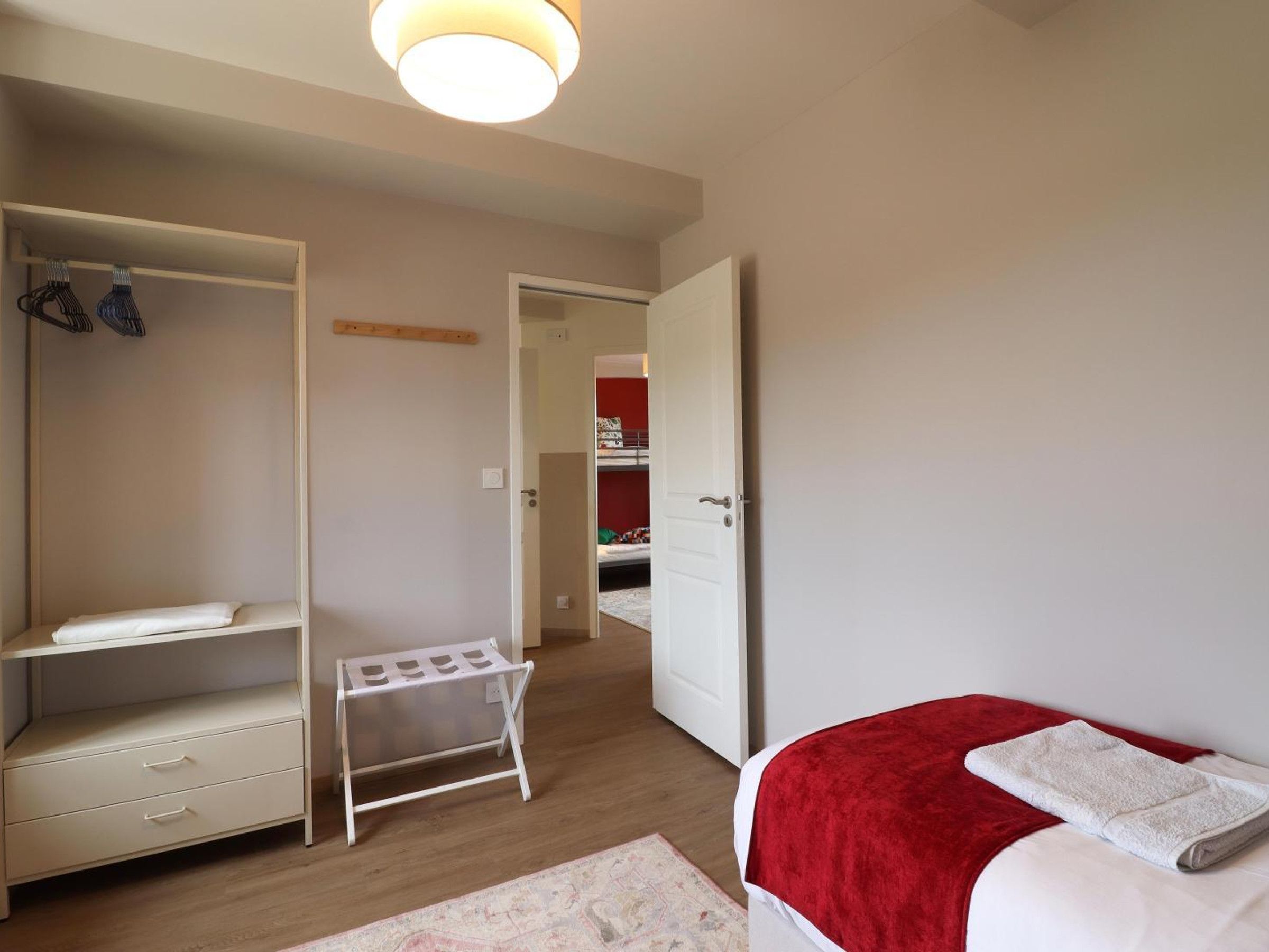 A bedroom with a bed, a wardrobe, a drying rack, and a door leading to another room.