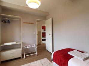 Une chambre à coucher comprenant un lit, une armoire, un étendoir et une porte donnant sur une autre pièce.