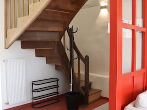 Un escalier en bois avec une rampe en métal, une étagère en métal noir et une poubelle noire.