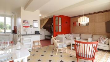 Une cuisine moderne avec un coin repas, un escalier et un salon comprenant un canapé et des fauteuils.