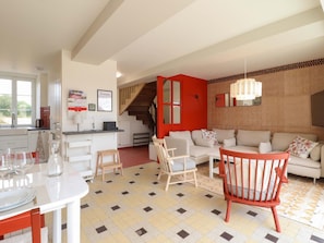 A modern kitchen with a dining area, a staircase, and a living room with a sofa and chairs.