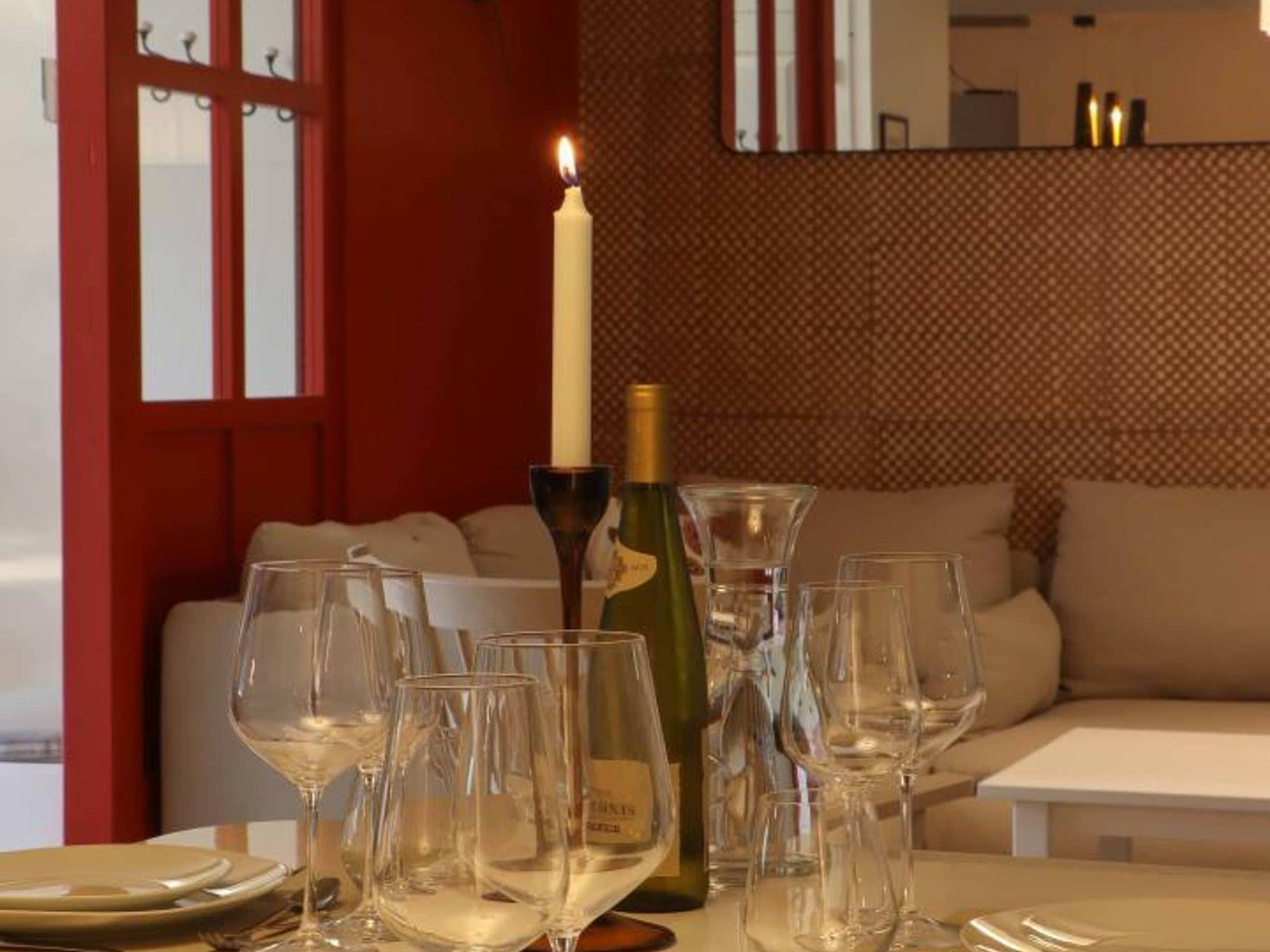 Une table  à manger avec des verres à vin, une bouteille et une bougie allumée.