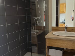 A modern bathroom with a glass shower enclosure, a sink with a wooden countertop, and a mirror reflecting the room. - Charming studio with parking - 3 guests, near slopes (Le Lioran)