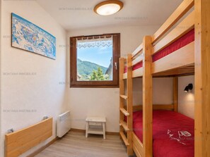 A room with bunk beds, a small table, a radiator, a window with a view of mountains, and a painting on the wall. - Quiet studio with parking - 4 guests (Le Grand-Bornand)