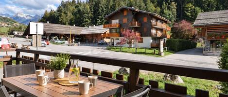 An outdoor seating area with wooden tables and chairs, overlooking a mountain landscape with a building in the background.