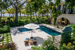 A swimming pool with lounge chairs and a table, surrounded by lush greenery and palm trees. - Beautiful beachfront villa with Spanish architecture (Savegre)