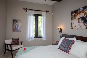 A bedroom with a bed, a chair, a window with curtains, a painting, and a wall-mounted light fixture. - Exquisite Spanish Colonial Beachfront Villa: lush gardens    & swimming pool (Savegre)
