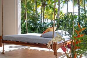 A hammock bed with a grey mattress and pillows, suspended by ropes, in a room with a tiled floor and surrounded by lush greenery. - Beautiful beachfront villa with Spanish architecture (Savegre)