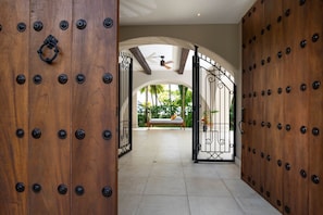 A hallway with a wooden door and a gate leading to a patio area with a bench and potted plants. - Exquisite Spanish Colonial Beachfront Villa: lush gardens    & swimming pool (Savegre)