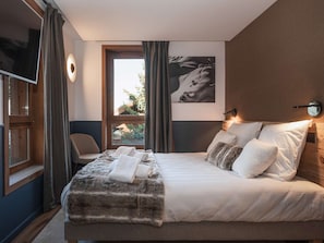 Ein Hotelzimmer mit einem Bett, einem Sessel, einem Fenster mit Vorhängen, einer Wandleuchte und einem Bild.