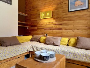 A cozy room with a wooden wall, a sofa with patterned cushions, and a table with cups. - Apartment mountain view - 4 guests (Plagne Bellecôte)