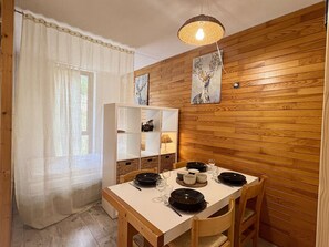 A dining area with a wooden wall, a white table, and a ceiling light fixture. - Apartment mountain view - 4 guests (Plagne Bellecôte)