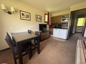 A compact living space with a dining table, chairs, a television, a kitchenette with a microwave, and a small cabinet. - Apartment mountain view in Belle Plagne - 4 guests (Belle Plagne)