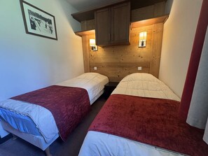 A room with two single beds, wooden headboard, wall-mounted lamps, and a framed picture on the wall. - Apartment mountain view in Belle Plagne - 4 guests (Belle Plagne)