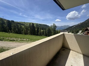 A concrete balcony with a view of a mountainous landscape, including a forested area and distant buildings. - Apartment mountain view in Belle Plagne - 4 guests (Belle Plagne)