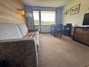 A furnished room with a sofa, a dining table with chairs, a television, and a window with a view. - Apartment mountain view in Belle Plagne - 4 guests (Belle Plagne)