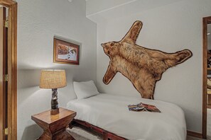 A bedroom with a large wall-mounted animal hide, a bed with white bedding, a wooden nightstand with a lamp, and a framed picture on the wall. - Mountain Retreat + Pet Friendly + Game Room + Community Hot Tub | Wild Iris Lodg (Edwards)