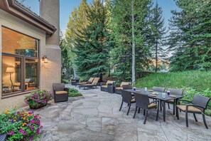 An outdoor patio with stone flooring, wicker furniture, and a view of a forested area. - Mountain Retreat + Pet Friendly + Game Room + Community Hot Tub | Wild Iris Lodg (Edwards)