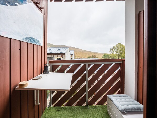 A small balcony with a white table, a cushioned bench, and a view of a hill and building in the background. - Modern studio, piste view - 4 guests (La Toussuire)