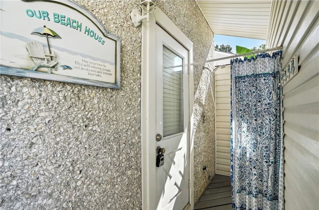 A beach-themed exterior with a sign reading 'OUR BEACH HOUSE,' a door, and a patterned curtain.