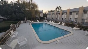 Una piscina rectangular con cubierta de madera, rodeada de sillas de descanso y mesas.