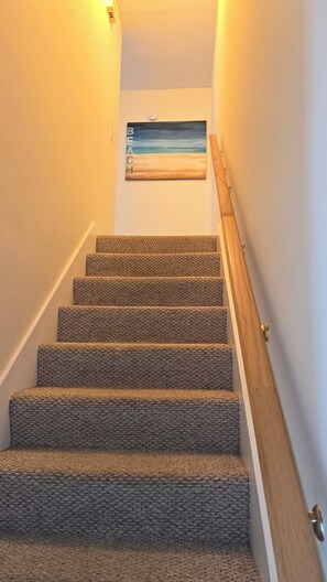 A carpeted staircase with a wooden handrail and a wall-mounted painting of a beach scene. - 3-bedroom two-story enchanted condo in terrific St. Simons Island (St. Simons Island)