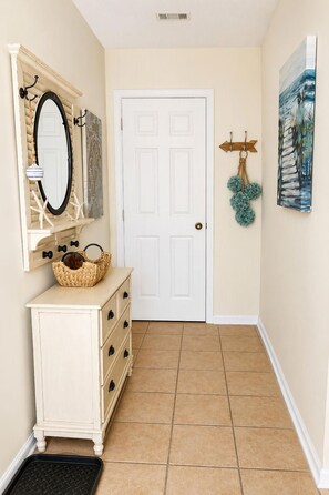 A hallway with a white door, a mirror, a basket on a dresser, and a painting on the wall. - 3-bedroom two-story enchanted condo in terrific St. Simons Island (St. Simons Island)