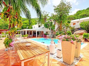 A poolside area with a wooden table, chairs, and potted plants. - Villa panoramic sea view - 12 guests (Saint-Martin)