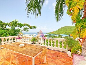 A terrace with a wooden table and chairs, surrounded by potted plants and a view of the sea and hills. - Villa panoramic sea view - 12 guests (Saint-Martin)