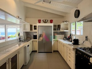 A kitchen with a stainless steel refrigerator, white cabinets, a window with a view, and a stove. - Villa panoramic sea view - 12 guests (Saint-Martin)