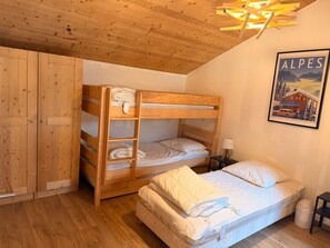 Un llit superposat amb capçalera de fusta, un llit individual amb matalàs i almoades, un armari de fusta i un quadre amb marc penjat a la paret.