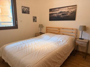 A bedroom with a wooden bed, two bedside tables with lamps, a window, and three framed pictures on the wall. - Lovely apartment near slopes - 5 guests (Pralognan-la-Vanoise)
