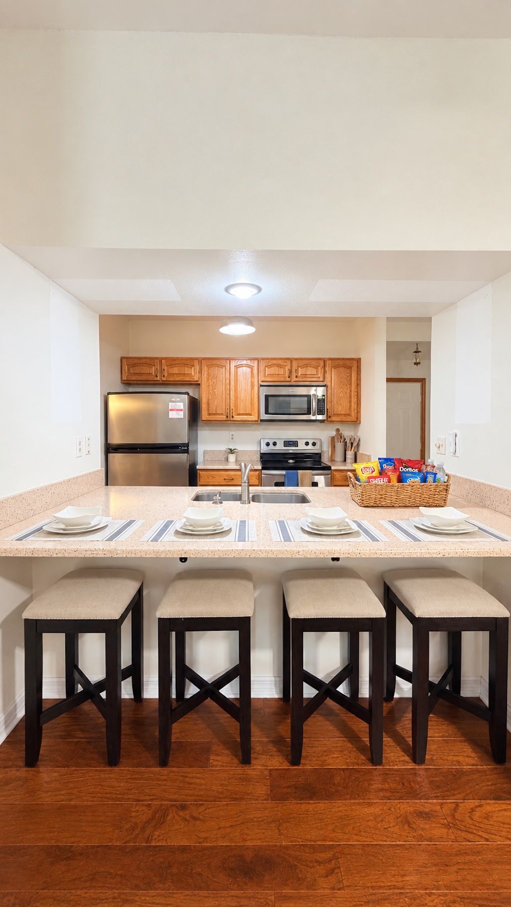 Cocina moderna con una isla central, electrodomésticos de acero inoxidable, armarios de madera y una zona de estar con taburetes.