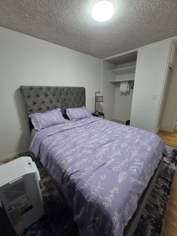 A bedroom with a tufted headboard, a bed with a floral-patterned bedspread, a bedside table with a lamp, and a heater on the floor.
