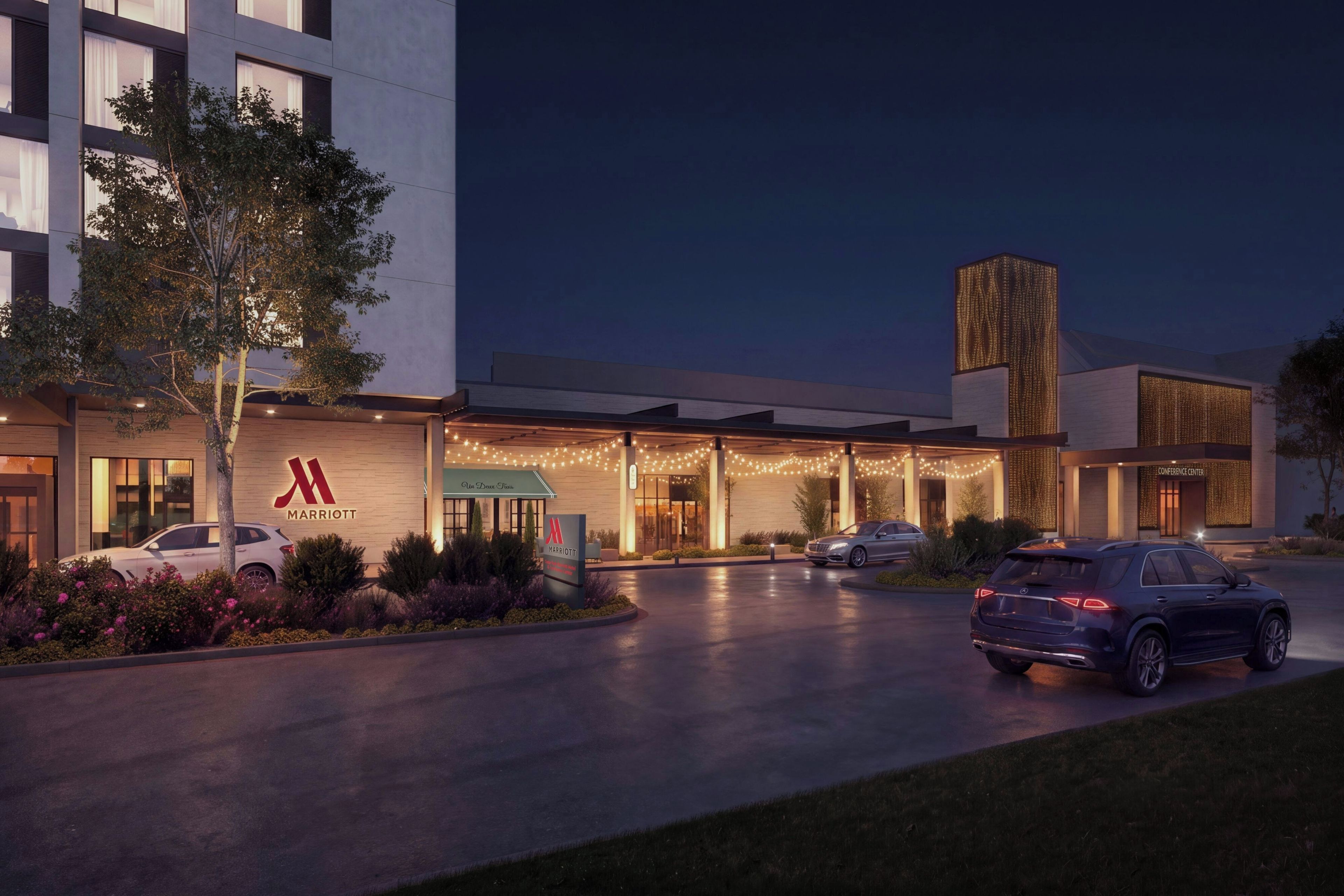 A Marriott hotel entrance with a modern design, a covered outdoor area, and a parking lot with cars.
