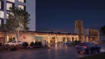 A Marriott hotel entrance with a modern design, a covered outdoor area, and a parking lot with cars.