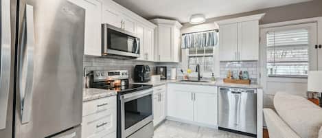 A modern kitchen with stainless steel appliances, white cabinetry, and a marble floor.