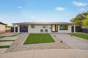 Una moderna casa a due piani con garage, un prato anteriore con un piccolo giardino e un vialetto lastricato.