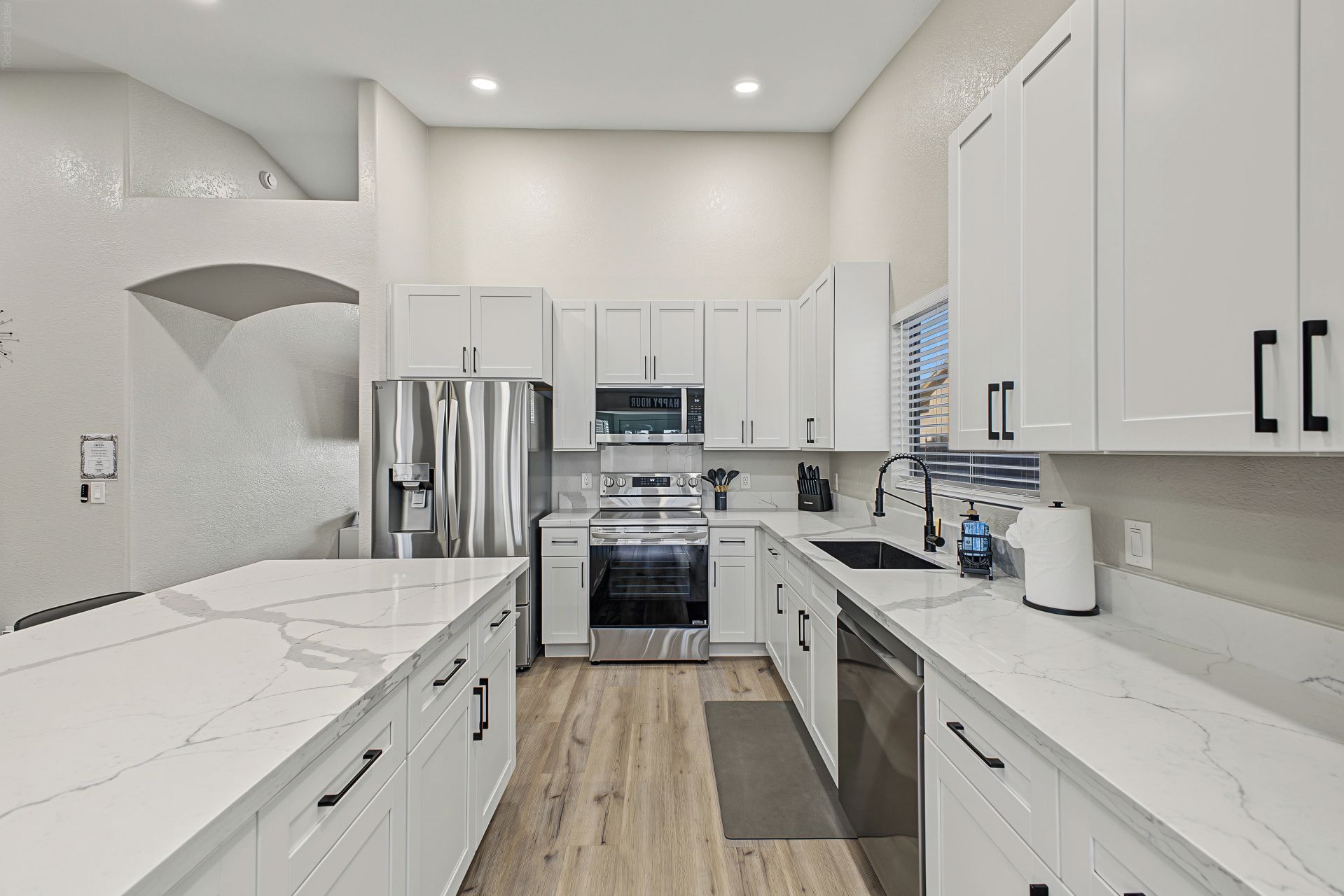 A modern kitchen with white cabinetry, stainless steel appliances, and a marble countertop.