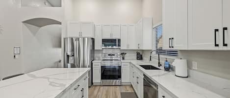 A modern kitchen with white cabinetry, stainless steel appliances, and a marble countertop.
