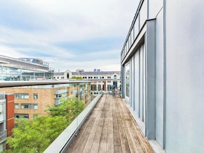 A balcony with a wooden floor, overlooking a cityscape with modern buildings and a clear sky. - Bright Westminster Duplex Apartment with Balcony (Greater London)