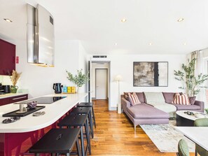 A modern kitchen with a central island, bar stools, and a dining area with a sofa and coffee table. - Bright Westminster Duplex Apartment with Balcony (Greater London)
