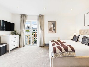 A bedroom with a bed, a TV, a dresser, and a window with curtains. - Bright Westminster Duplex Apartment with Balcony (Greater London)