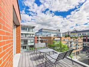 Een balkon met een tafel en stoelen, met uitzicht op een stadsgezicht met moderne gebouwen.