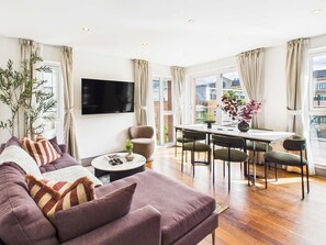 Een moderne woonkamer met een bank, een salontafel, een televisie en een eethoek met stoelen en een tafel.