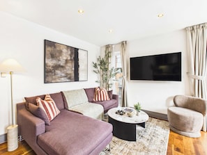 A modern living room with a sofa, armchair, coffee table, and a flat-screen TV. - Bright Westminster Duplex Apartment with Balcony (Greater London)
