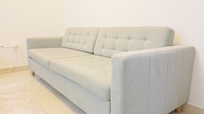 A light-colored sofa with a tufted backrest in a room with white walls and a tiled floor. - Boho Studio - Balcony & Sea View - Pool & Gym (Ajman)