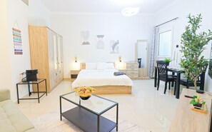 A modern hotel room with a bed, bedside table, a small coffee table, a desk, and a dining area. - Boho Studio - Balcony & Sea View - Pool & Gym (Ajman)
