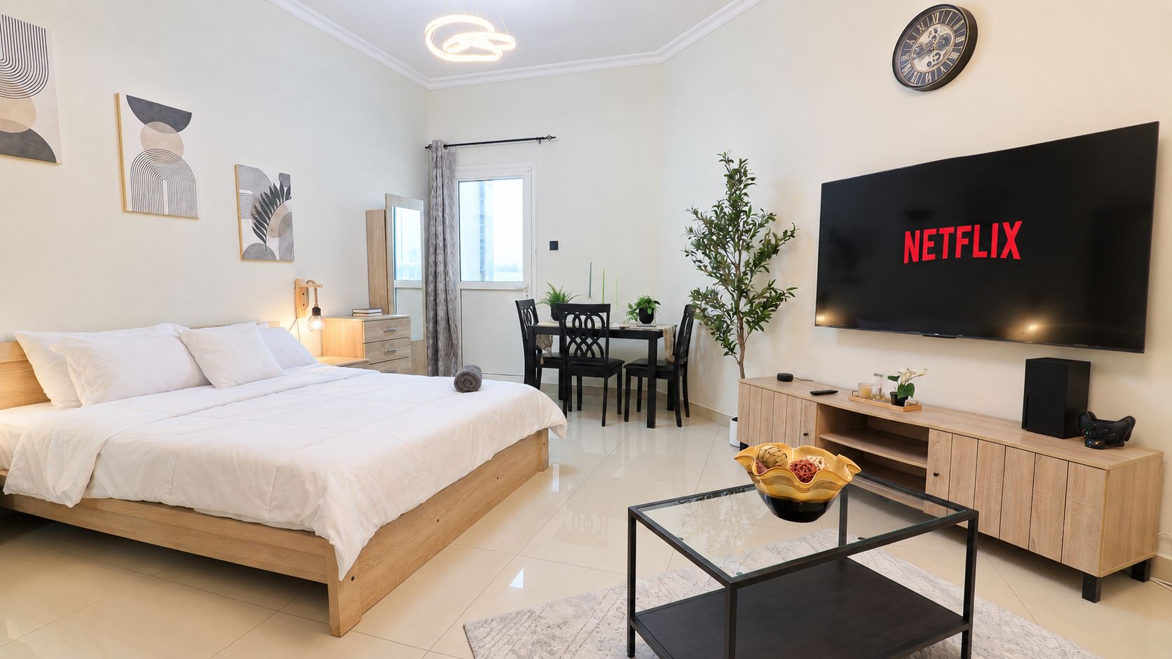 A modern bedroom with a large bed, a TV, a dining area, and artwork on the walls.