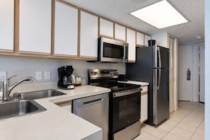 A modern kitchen with stainless steel appliances, a microwave, a refrigerator, and a coffee maker. - Bay Watch Resort 1519 (North Myrtle Beach)